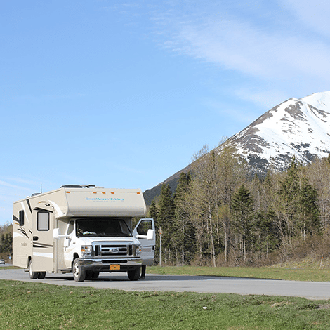 RV stopped on pavement with doors open and beautiful snowy mountain in background
