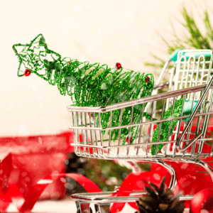 Christmas decorations and wrapping materials on surface surrounding a small shopping cart