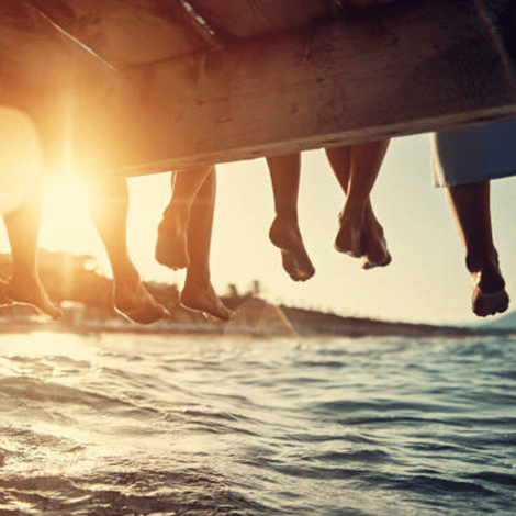 People sitting on pier dock with feet hanging off edge with the ocean beneath them