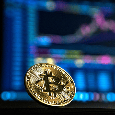Bitcoin sitting on edge of surface with computer screen behind