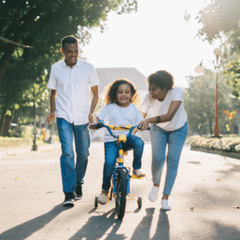 Family showing young daughter how to ride a bike