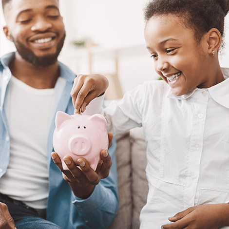 Father and daughter smiling while daughter drops coin into piggybank