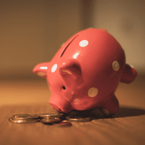 Piggy bank tipped over on its nose with coins laying in front of it