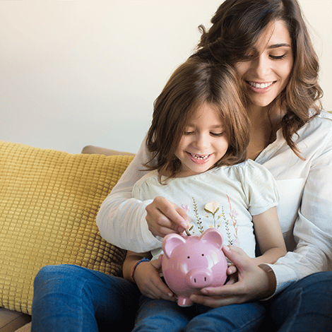Mother and daughter sitting on couch placing coin in piggybank